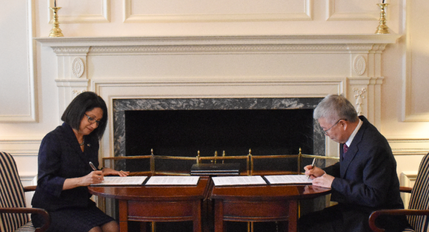 A woman and a man at a wooden table signing documents