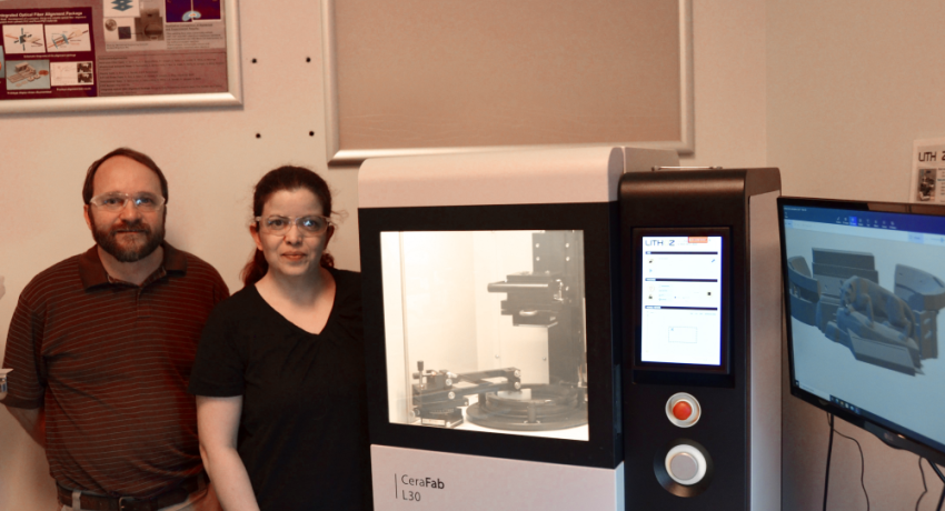 A man and a woman standing next to a 3D printer in a lab