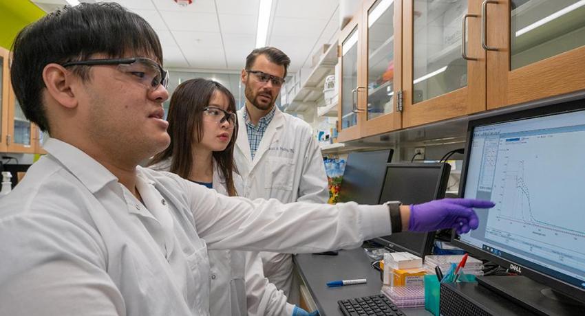 Three people reviewing lab results on a computer screen.