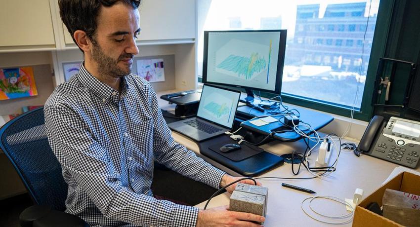 An individual sits at a desk holding two rocks attached to lab instruments.